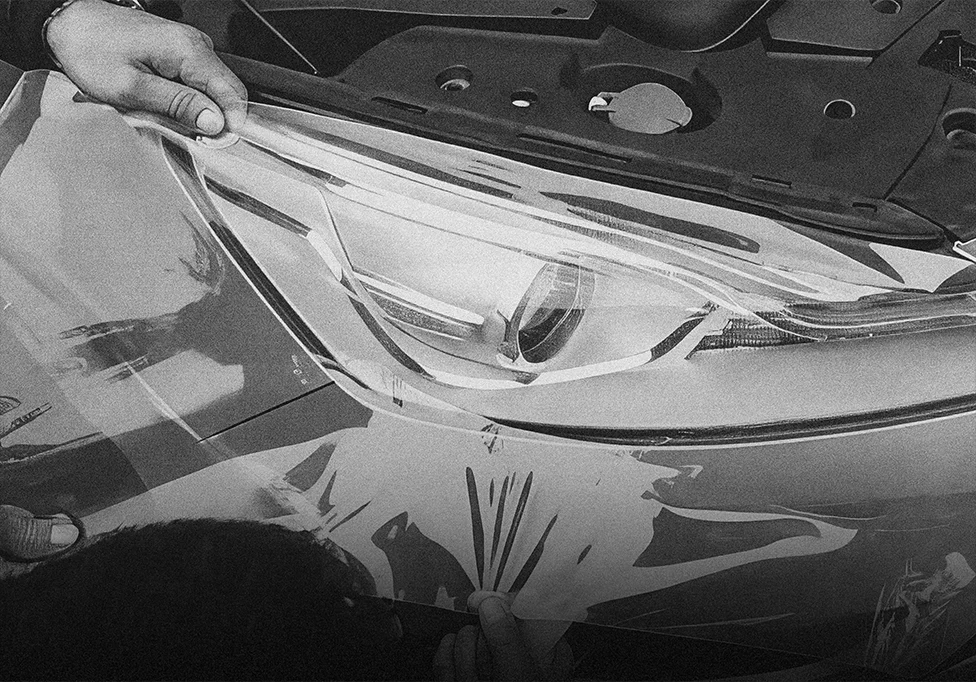 Installer positioning protection film over a headlight